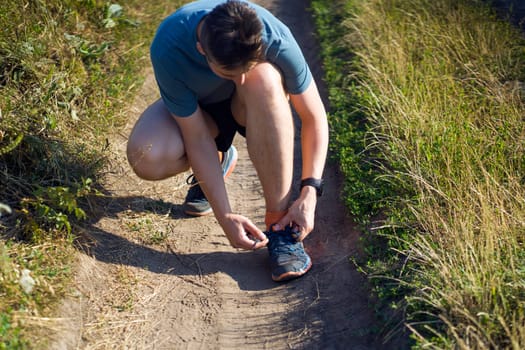 Close-up view of a young man tying his laces on his sneakers, getting ready for training and jogging along the trails in the park.