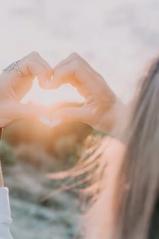 A woman's hand is holding a heart shape, with the sun shining on it. Concept of love and warmth, as the sun symbolizes happiness and positivity. The heart shape represents the bond between two people
