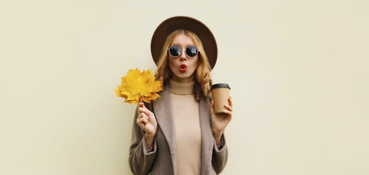 Autumn portrait of beautiful happy surprised woman with yellow maple leaves, stylish emotional girl holding cup of coffee posing isolated on brown background