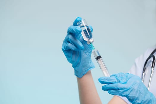 The doctor's hand wears a medical glove holding a syringe while taking a liquid vaccine from a vial about to be injected. Injection vaccination concept