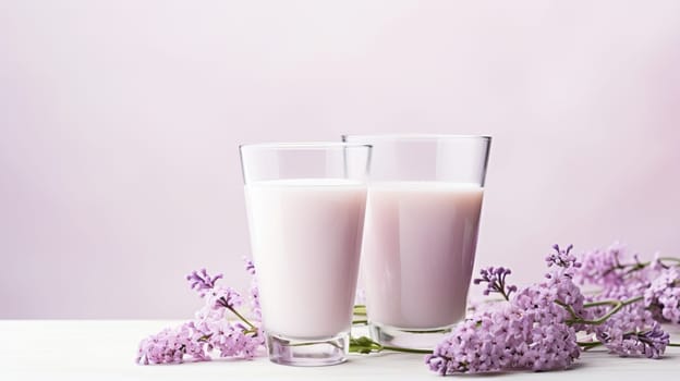 Two glasses of creamy strawberry milkshake with fresh lilac flowers on pink background. Concept of refreshing sweet dairy drink, summer dessert, and floral decoration.