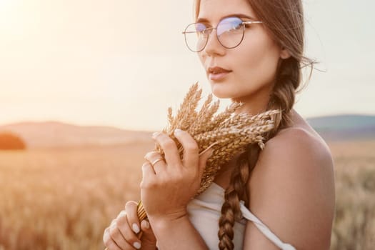 A woman is holding a bunch of wheat in her arms. The wheat is dry and brown, and the woman is wearing a white dress. The scene is set in a field, and the woman is posing for a photo