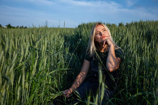 In the tranquil expanse of a rustic wheat field, a female farmer squats, holding a wheat stalk in one hand, contemplatively placing it near her lips. With sun-kissed skin and clad in work attire, she embodies the essence of rural life. Her expression is one of introspection, leaving viewers to ponder whether she is content with the harvest or harbors concerns. She is looking at the blue sky. The vibrant green hue of the wheat stalk contrasts against the golden tones of the field, adding depth to the scene. Against the backdrop of the sprawling countryside, her presence evokes a sense of agricultural tradition and connection to the land. This image captures the quiet moments of farming, where contemplation mingles with the labor of the harvest. As she gazes thoughtfully upon the wheat, her blonde hair softly frames her face, enhancing the rustic charm of the scene