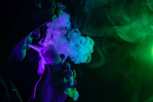 male vaper holding vape electronic cigarette close-up on background of colored smoke, concept of harm of smoking