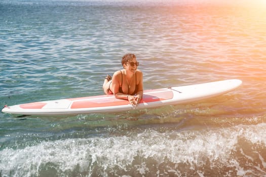 Woman sup sea travel. Sports girl on a surfboard in the sea on a sunny summer day. In a black bathing suit, he sits on a sapa in the sea. Rest on the sea