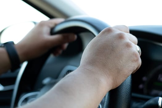 Auto concept. Male hands firmly hold the black steering wheel of a car. The driver moves on the highway during the day. Close-up. Soft focus.