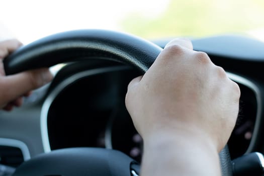 Auto concept. Male hands firmly hold the black steering wheel of a car. The driver moves on the highway during the day. Close-up. Soft focus.