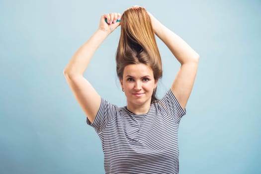 Beautiful brown-haired woman brushing her beautiful shiny hair with hairbrush on blue background