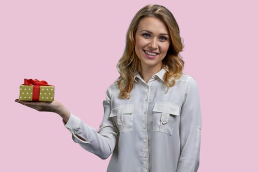 Happy young attractive lady holding yellow gift box with red ribbon. Isolated on pink background.