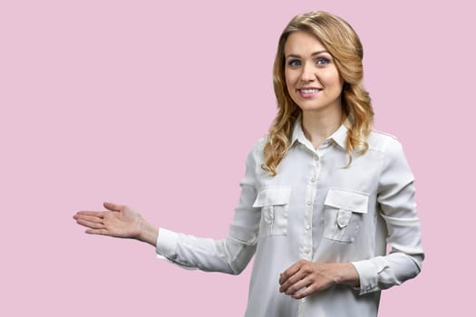 Portrait of a young blonde woman pointing at copy space with her right hand. Isolated on pink background.