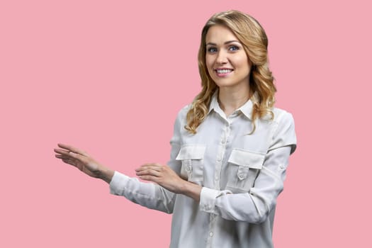 Attractive young blonde woman pointing at copy space with both hands. Isolated on pink background.