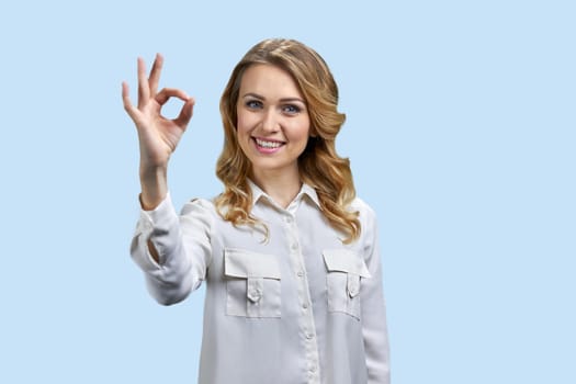 Portrait of a young blonde woman showing okay gesture. Cute smiling woman isolated on blue.