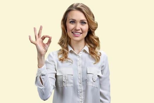 Portrait of a young blonde businesswoman showing ok gesture. Isolated on yellow background.