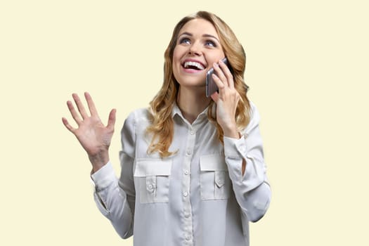 Young expressive lady is talking on mobile phone. Isolated on pastel yellow background.