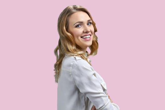 Smiling cheerful blonde businesswoman in half-turned pose. Isolated on pink background.
