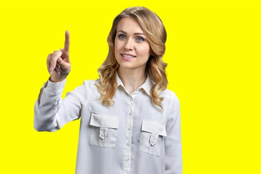 Portrait of blond woman is touching transparent virtual screen. Vivid yellow background.