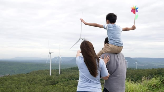 Concept of progressive happy family enjoying their time at the wind turbine farm. Electric generator from wind by wind turbine generator on the country side with hill and mountain on the horizon.