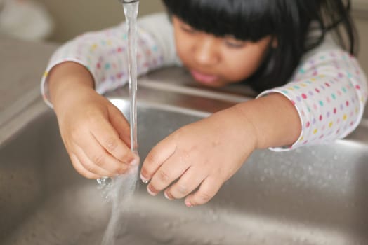 child washing hands with water at kitchen sink .