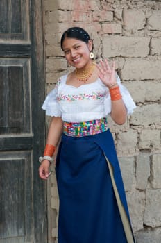 pretty indian girl waving and smiling at the camera next to her humble mud house and old door.Hispanic Heritage Month. High quality photo