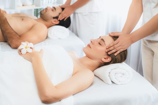 Caucasian couple enjoying relaxing anti-stress head massage and pampering facial beauty skin recreation leisure in dayspa modern light ambient at luxury resort or hotel spa salon. Quiescent