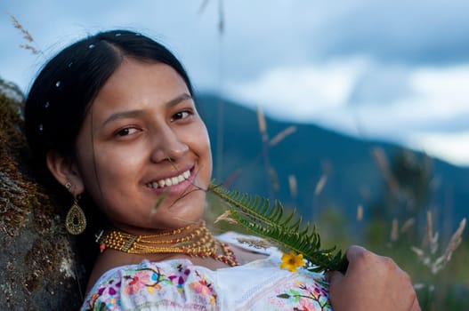 close-up copy-space of beautiful indigenous woman leaning on a rock with traditional otavalo dress, gold necklace and plants in her hands.Hispanic Heritage Month. High quality photo