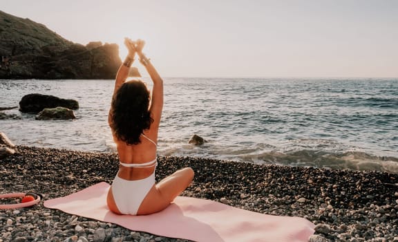 Young woman in swimsuit with long hair practicing stretching outdoors on yoga mat by the sea on a sunny day. Women's yoga fitness pilates routine. Healthy lifestyle, harmony and meditation concept.