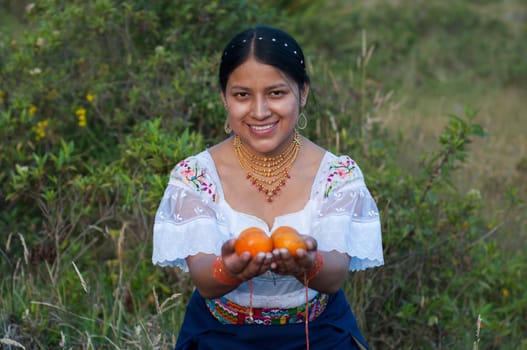 beautiful young indian girl looking at the camera very happy and smiling, dressed in traditional latin american clothes showing some oranges just picked from her harvest. Hispanic Heritage Month. High quality photo