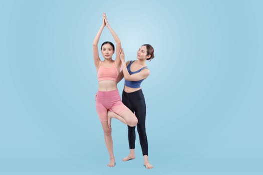 Asian woman in sportswear doing yoga exercise in standing pose with her trainer or yoga buddy. Healthy body care and meditation yoga lifestyle in full shot on isolated background. Vigorous