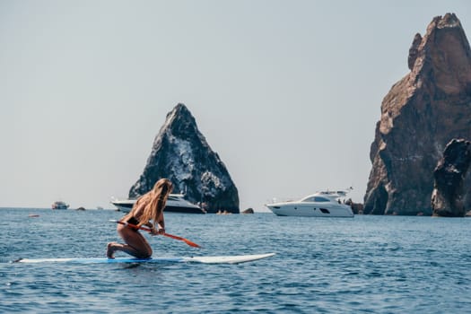 Close up shot of beautiful young caucasian woman with black hair and freckles looking at camera and smiling. Cute woman portrait in a pink bikini posing on a volcanic rock high above the sea