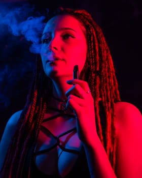 Caucasian girl with dreadlocks smokes a vape in red blue light