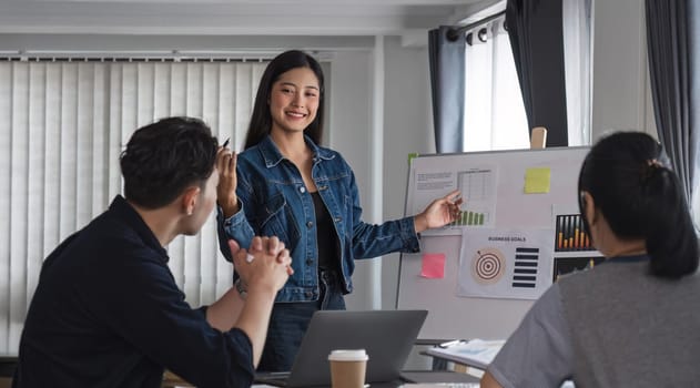 Young businesswoman explains work plan in meeting to teammates in conference room.