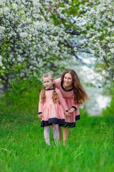 mother and daughter walk through a blooming apple orchard