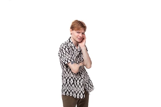 young tired caucasian man with red hair with a tattoo is dressed in a summer black and white shirt on a background with copy space.