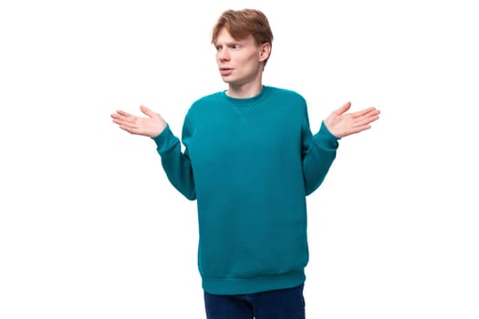portrait of a confused slender young european man with red hair in a blue sweater.