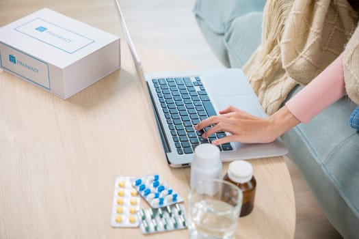 Business female sick she taking pills for flu while work with laptop keyboard, Asian sick woman covered blanket suffering from covid-19 virus but still working at home with laptop computer