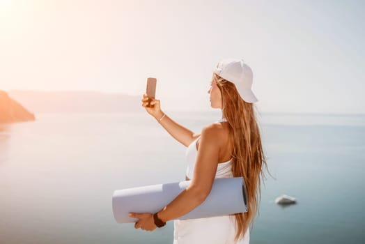 Young woman with black hair, fitness instructor in pink sports leggings and tops, doing pilates on yoga mat with magic pilates ring by the sea on the beach. Female fitness daily yoga concept