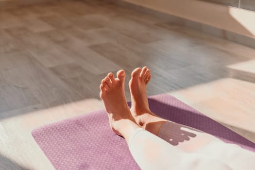 Young woman with long hair in white swimsuit and boho style braclets practicing outdoors on yoga mat by the sea on a sunset. Women's yoga fitness routine. Healthy lifestyle, harmony and meditation