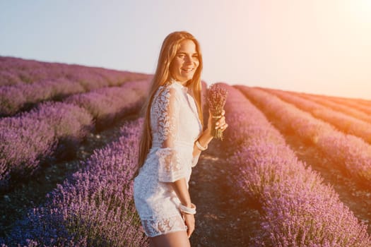 Close up portrait of young beautiful woman in a white dress and a hat is walking in the lavender field and smelling lavender bouquet.