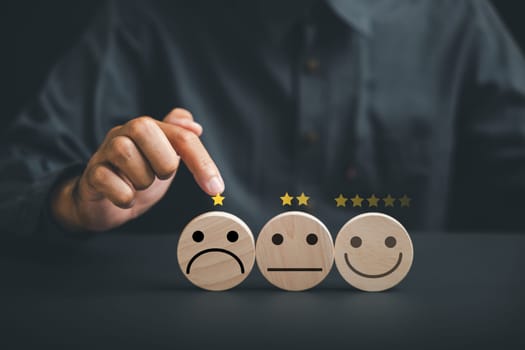 Negative customer experience concept. Hand holding wooden block with sad face icon on circle wooden table, symbolizing unhappiness and bad service. Dissatisfied client expressing dissatisfaction.