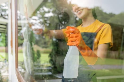 Young Asian housewife cleaning window glass with rags and detergent spray, cleaning house on the weekend.