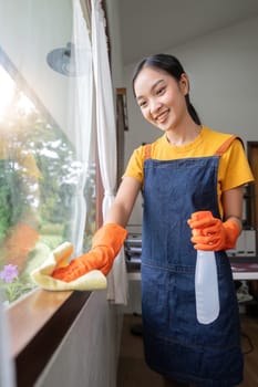 Young Asian housewife clean window glass with rag and detergent spray, cleaning house on the weekend.