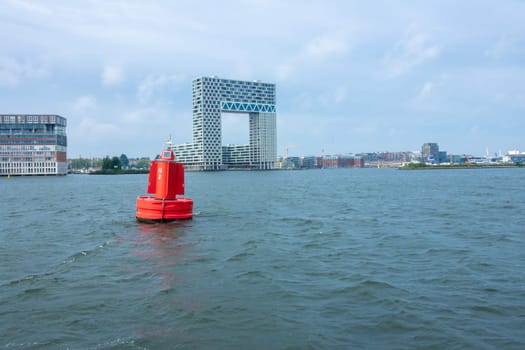 Netherlands. Summer day in Amsterdam. Buoy on the Amstel River and an office building on the bank
