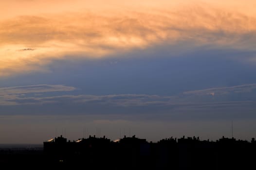 Setting sun illuminated the clouds high in the sky above the city rooftops