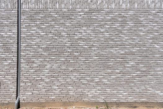 fragment Gray textured brick wall with built-in pipe for collecting rainwater from the roof, long and narrow modern bricks, horizontal Textured stone background, brickwork outside new building,