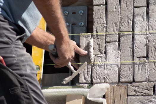 close up of builder using level and yellow cord to glue grey brick with cement to masonry on facade of new house, quality work concept,