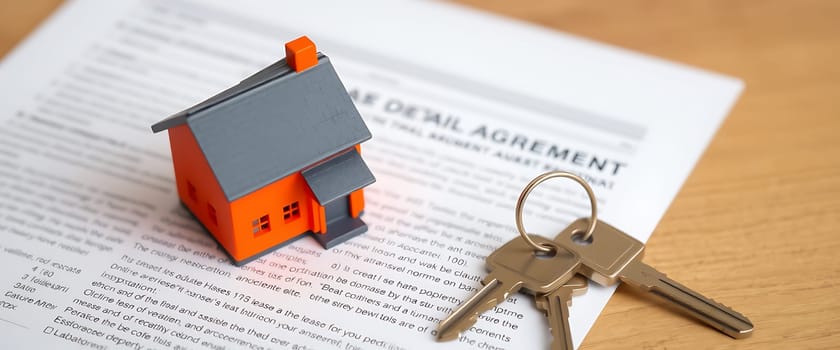 A small orange model house sits next to keys on top of a rental agreement, highlighting the process of securing a property lease in a cozy setting.