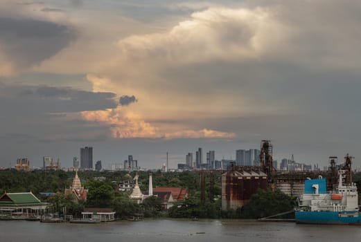 Bangkok, Thailand - 14 Aug, 2024 - View of green forest area of Bang kachao overlooking Thai temples, Petroleum refinery and cargo ship alongside the Chao Phraya River on background of Dramatic sky in the city of Bangkok before Sunset. use it as your wallpaper, poster and banner design, Selective focus.
