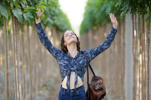 A cheerful and joyful woman stands confidently in a vibrant and lush green aisle, with her arms raised high in pure joy, surrounded by stunning, verdant foliage and towering trees