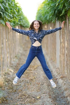 A cheerful young woman jumps joyfully in a picturesque vineyard, surrounded by vibrant green grapevines, embodying a true sense of freedom, joy, and pure happiness in natures beauty and bounty