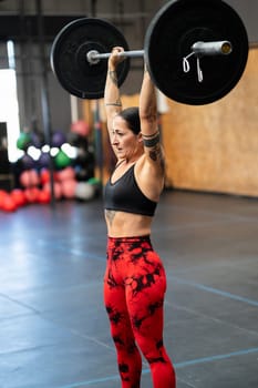 Vertical photo of a mature sportive and strong woman lifting weights alone in a gym